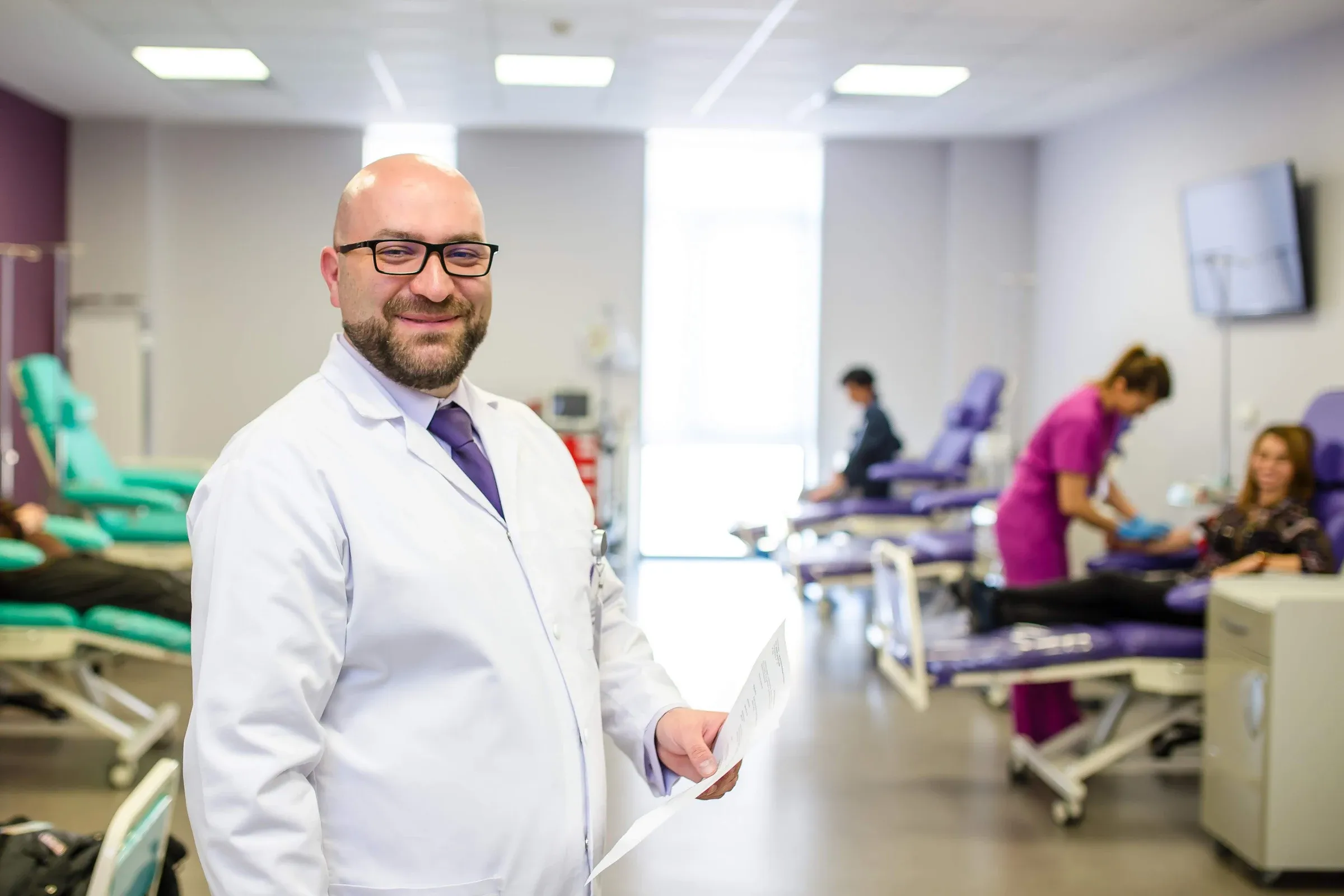 Dr. Andrei Ungureanu în sala de tratament oncologic, cu o asistentă îngrijind un pacient în fundal